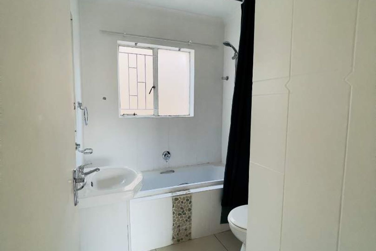 A functional bathroom featuring a pedestal basin, bathtub with shower attachment, and tiled finishes throughout.