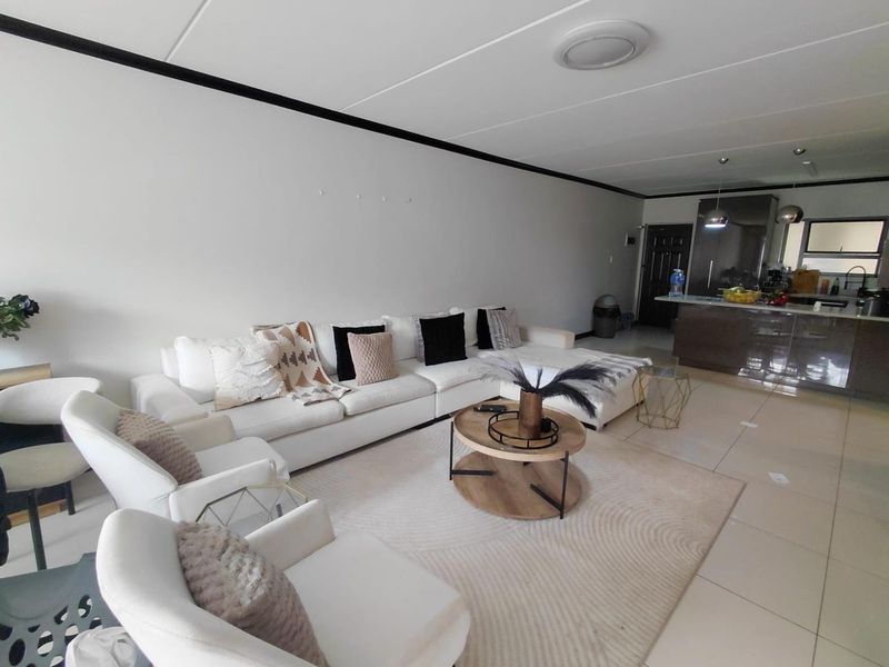 Spacious open-plan living area featuring tiled flooring, a modern kitchen with an island, and integrated lighting, creating a functional and cohesive living space.