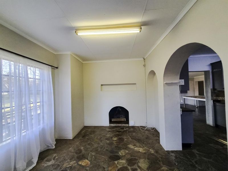 An empty living room featuring a traditional fireplace, unique stone flooring, and architectural archways leading to the kitchen area.