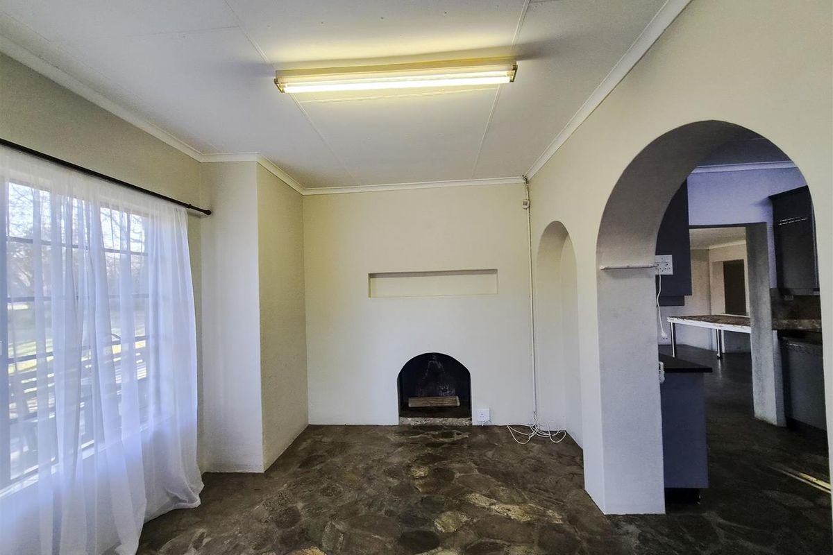 An empty living room featuring a traditional fireplace, unique stone flooring, and architectural archways leading to the kitchen area.