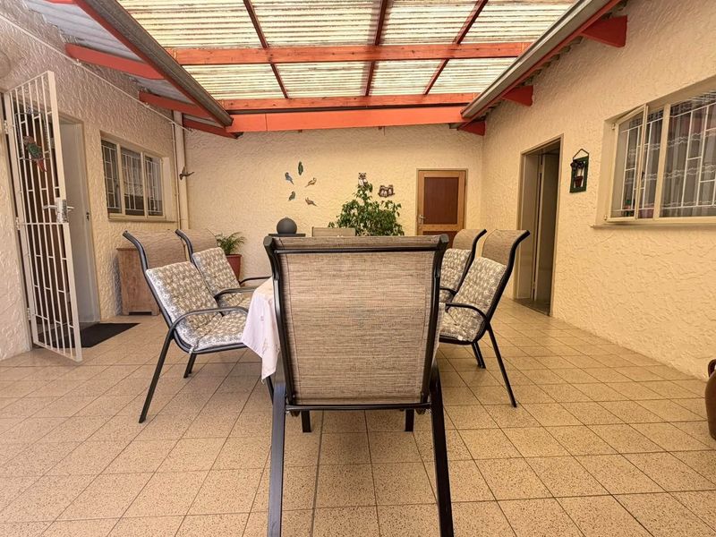 A covered outdoor patio area featuring tiled flooring, a translucent roof with timber beams, and textured walls, providing a functional space for outdoor dining.