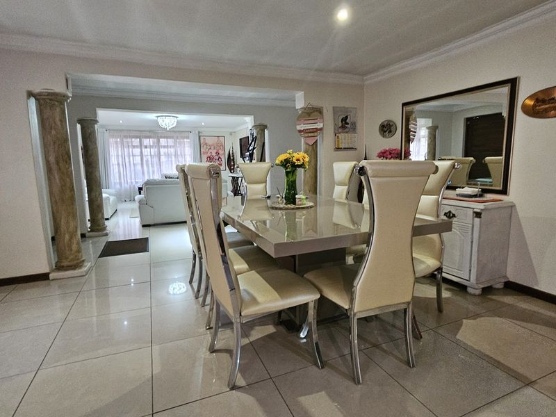 Spacious dining area featuring polished porcelain floor tiles, decorative columns, and elegant cove ceiling molding, flowing into an adjacent living space.