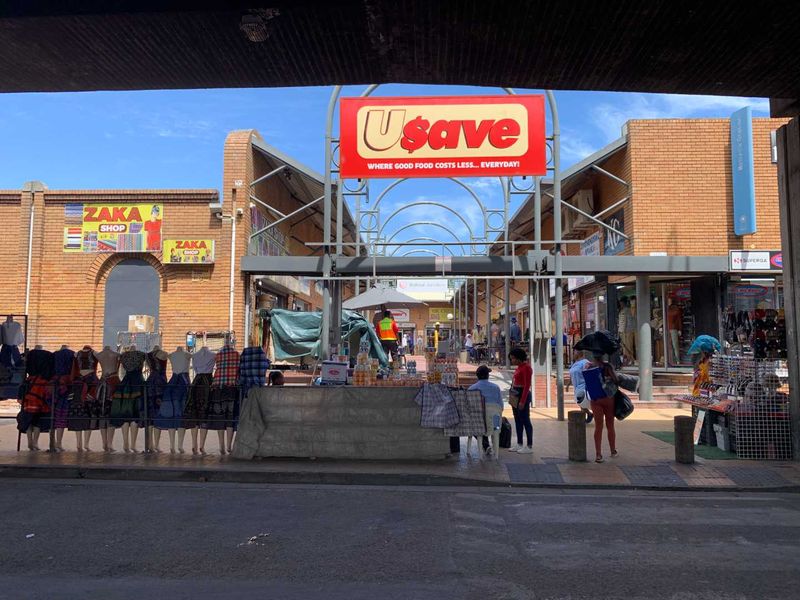 Front view of a retail shopping center entrance featuring brick construction, steel structural elements, and prominent commercial signage.