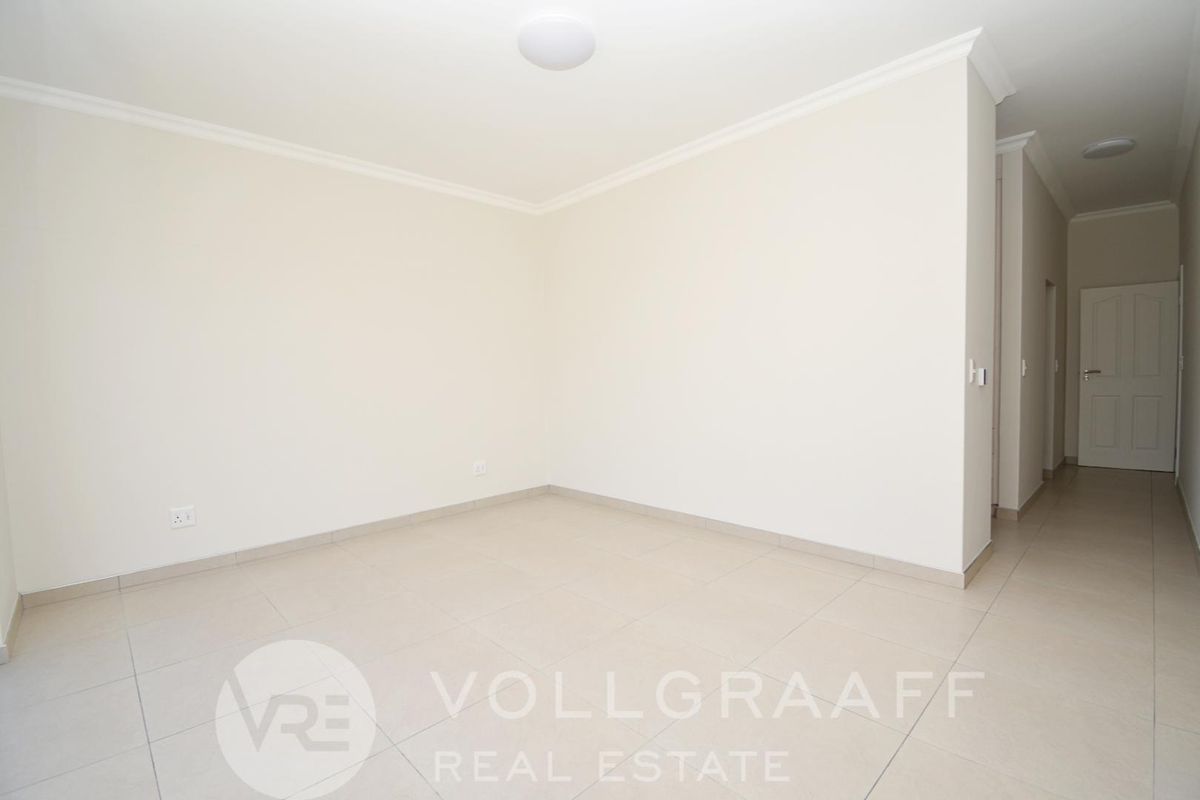 A bright, neutral-toned empty room featuring tiled flooring, crown molding, and a clean, minimalist aesthetic suitable for various living arrangements.