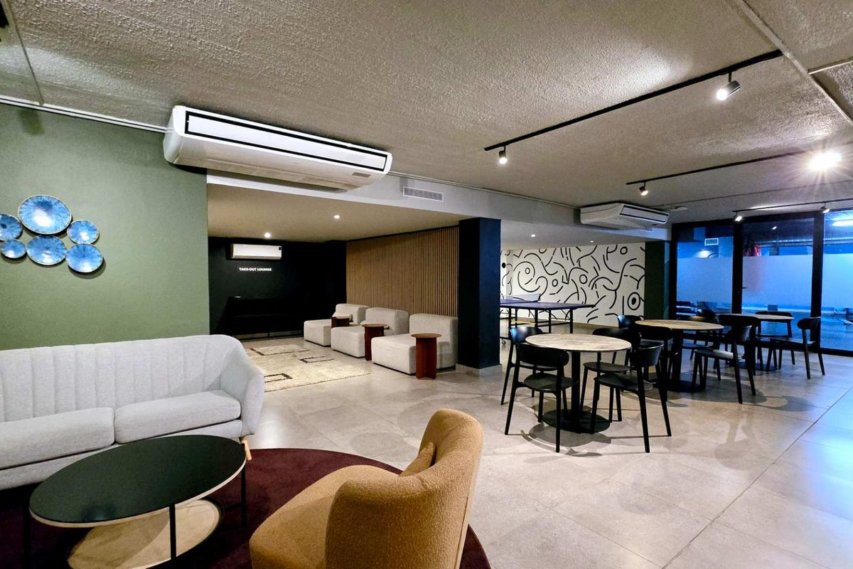 A spacious, modern communal lounge area featuring tiled floors, track lighting, multiple air conditioning units, and stylish timber wall accents.