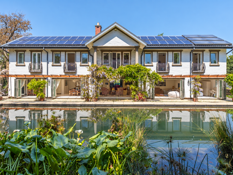 A stunning rear elevation of a two-story residence featuring solar panels, expansive bi-fold doors opening to a swimming pool, and manicured garden surroundings.