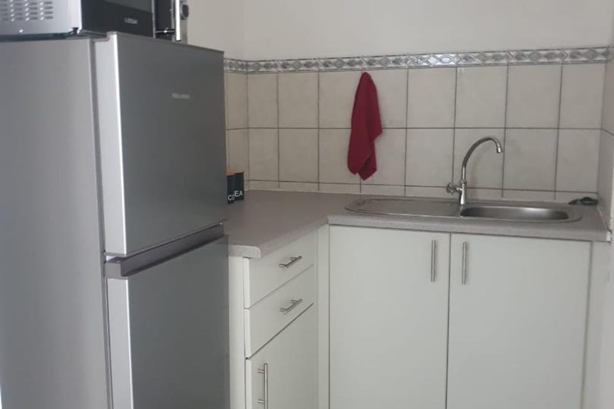 A compact office kitchenette featuring white cabinetry, a stainless steel sink, tiled backsplash, and tiled flooring.