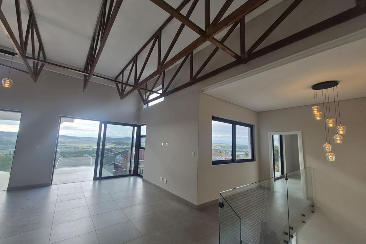 Spacious open-plan living area featuring high ceilings with exposed timber trusses, large sliding doors leading to a balcony, and modern glass balustrades.