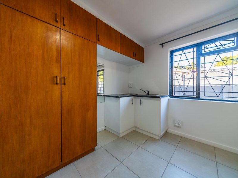 A compact kitchen area featuring built-in wooden cabinetry, a small sink, and tiled flooring, offering a functional space with natural light.