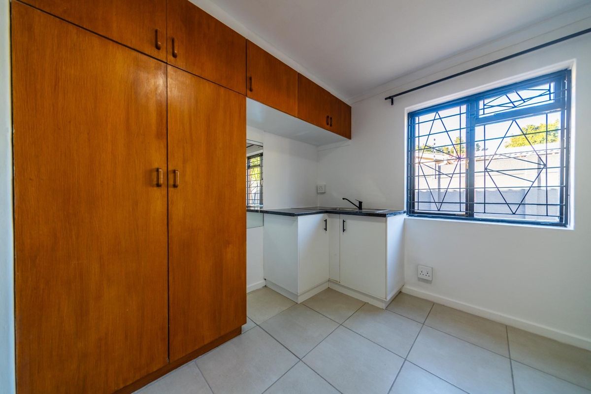 A compact kitchen area featuring built-in wooden cabinetry, a small sink, and tiled flooring, offering a functional space with natural light.