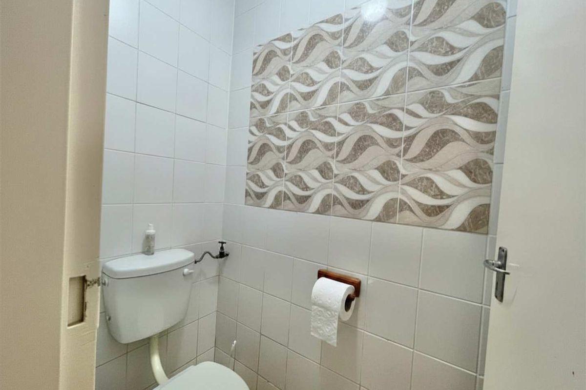 A compact guest bathroom featuring white wall tiles, a decorative accent tile wall, and a standard white toilet suite.