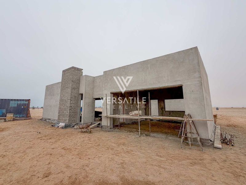An exterior view of a property currently under construction, featuring a concrete shell structure and a brick chimney stack in a desert setting.