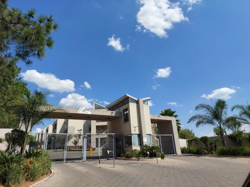 The main entrance gate and security access point for the apartment complex, featuring paved driveway and modern architectural design.