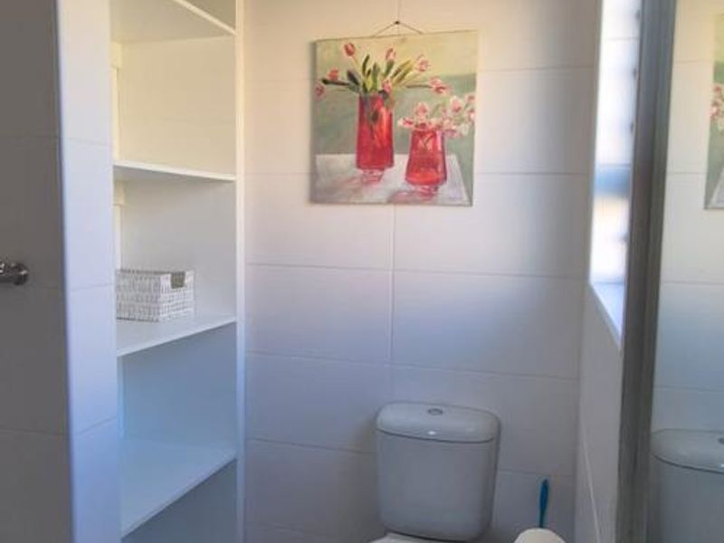 A clean and functional bathroom featuring white wall tiles, built-in shelving, a pedestal basin, and a toilet.