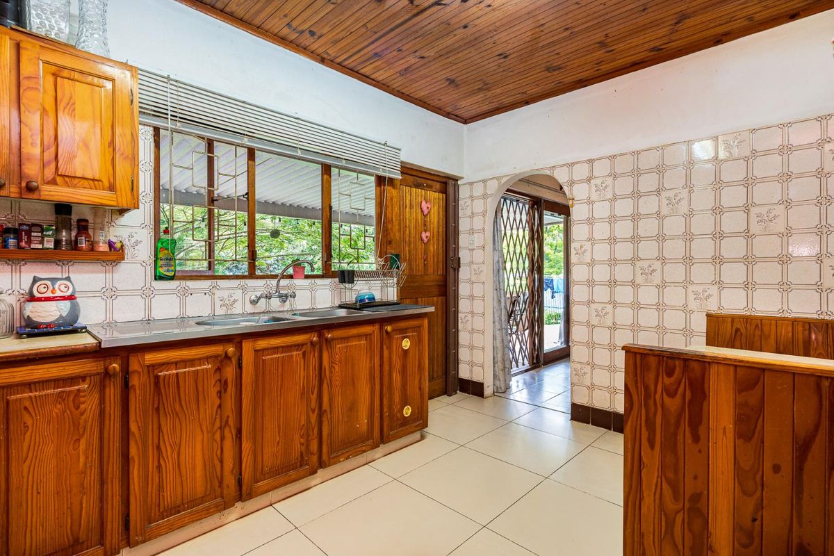 A dated kitchen featuring wooden cabinetry, tiled walls, and a wood-paneled ceiling, with direct access to an outdoor patio area.