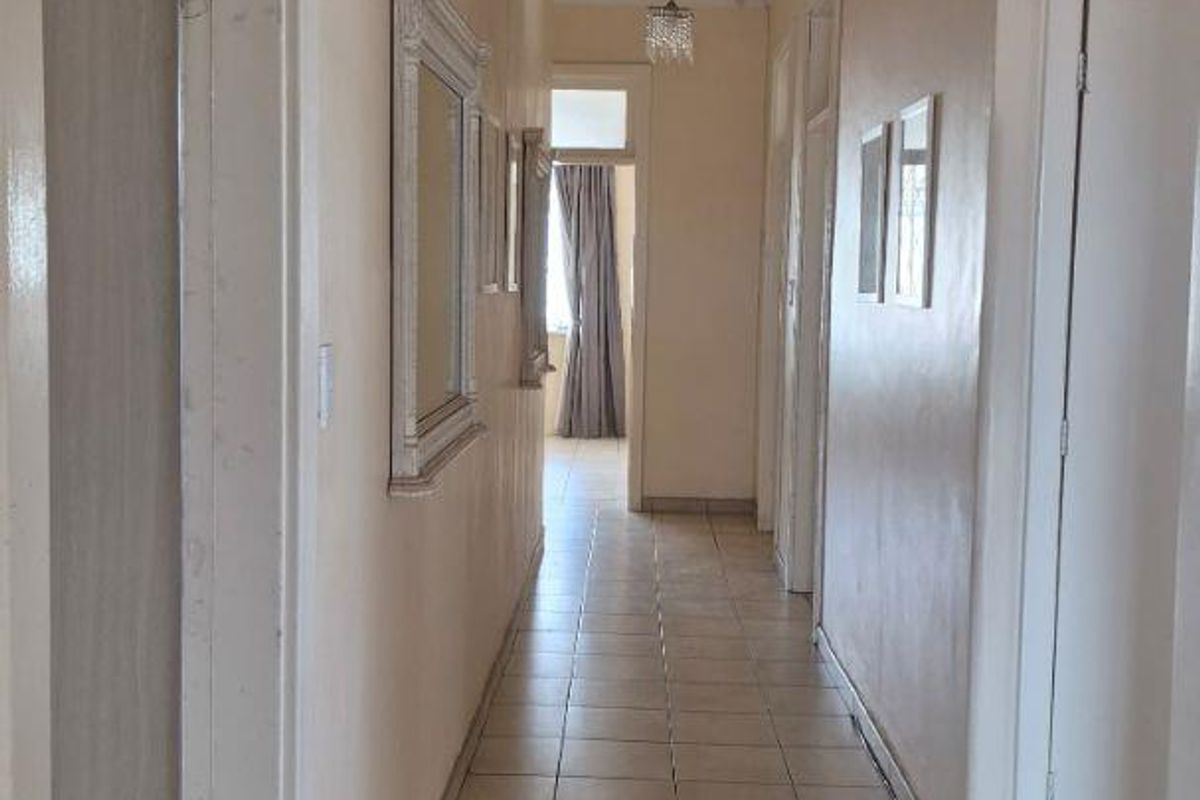 A long, tiled hallway connecting multiple rooms, featuring neutral wall tones and classic ceiling light fixtures.