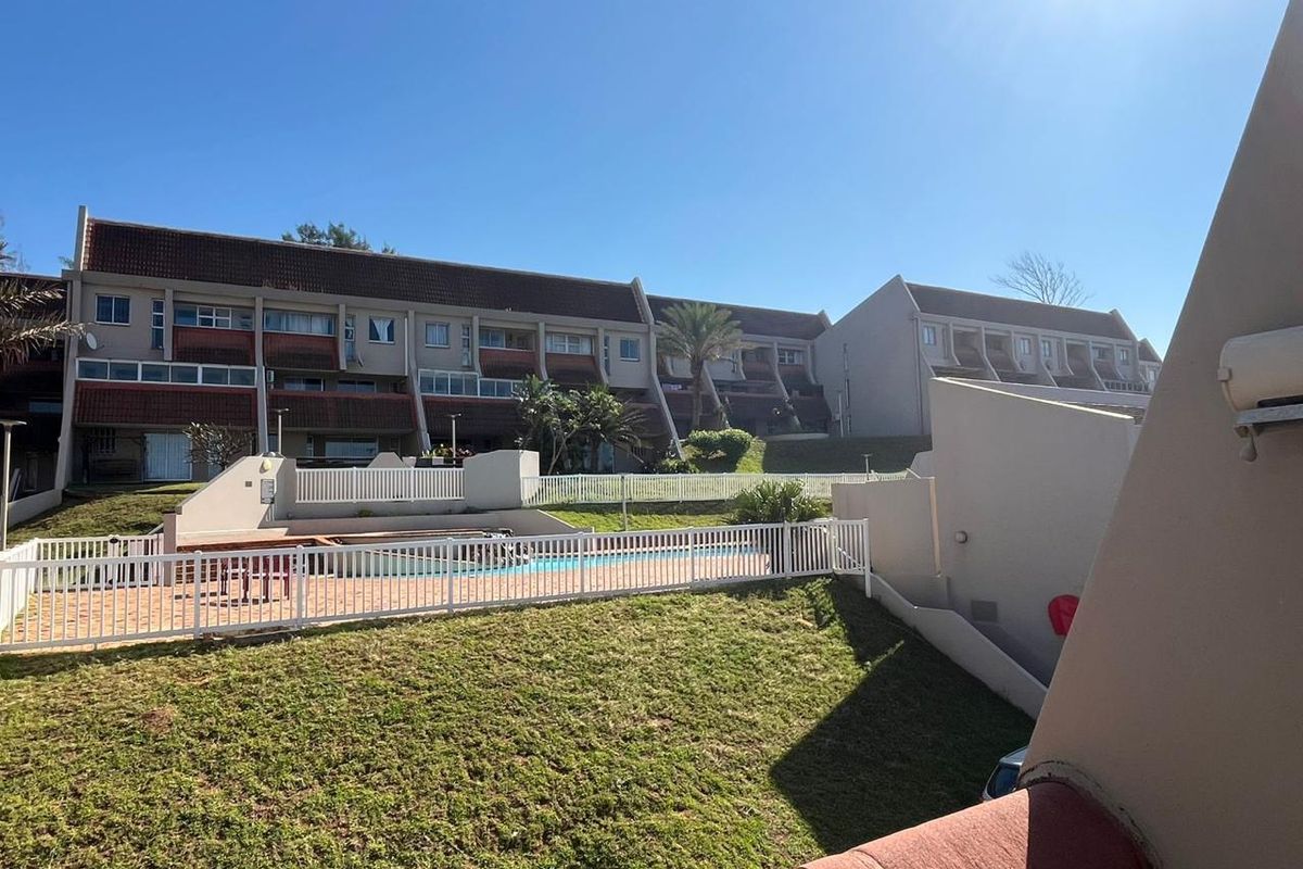 Exterior view of the apartment complex featuring a communal swimming pool, paved patio area, and well-maintained lawn space.