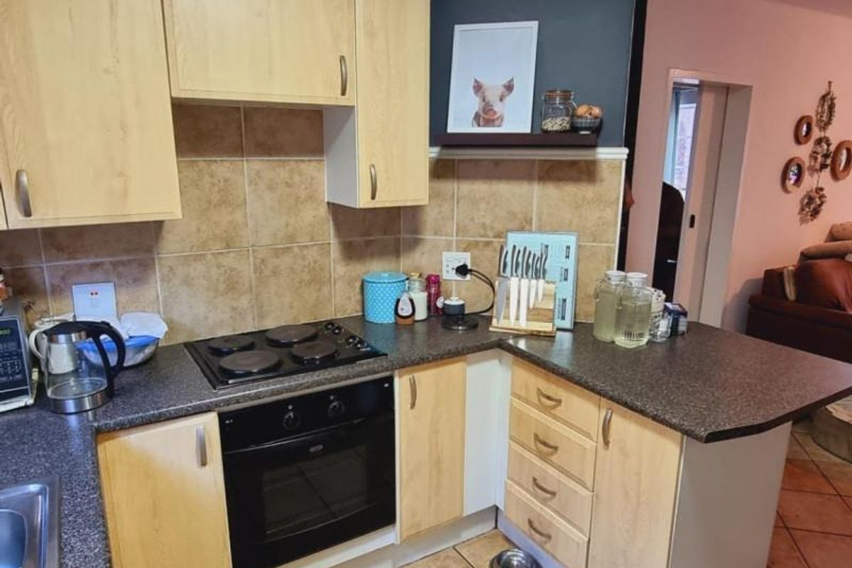 A functional kitchen featuring light wood-finish cabinetry, dark laminate countertops, a built-in electric oven and hob, and tiled backsplash.