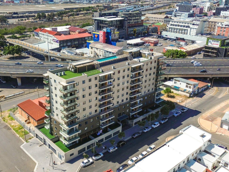 Aerial view of a modern apartment building featuring multiple balconies, a rooftop pool, and surrounding urban infrastructure.