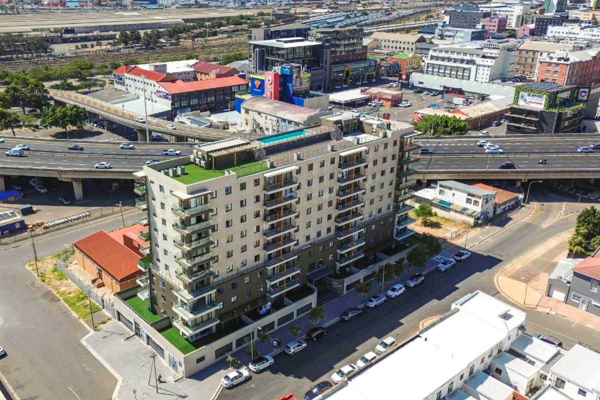 Aerial view of a modern apartment building featuring multiple balconies, a rooftop pool, and surrounding urban infrastructure.