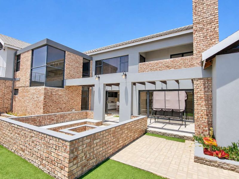 Spacious rear exterior featuring a brick facade, paved patio area with a built-in brick fire pit, and access to the home via sliding glass doors.
