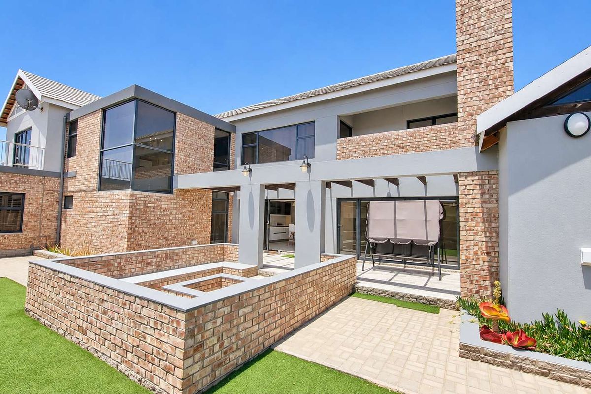 Spacious rear exterior featuring a brick facade, paved patio area with a built-in brick fire pit, and access to the home via sliding glass doors.