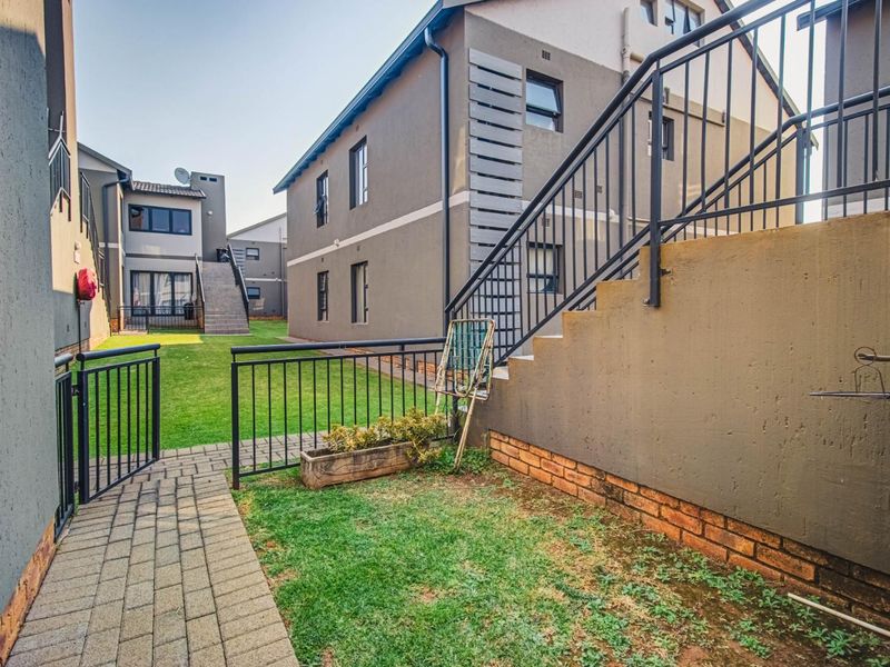 Rear exterior view of the townhouse complex featuring a paved walkway, communal lawn area, and external staircase with metal railings.