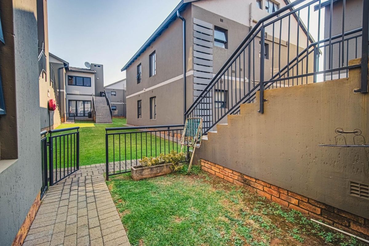 Rear exterior view of the townhouse complex featuring a paved walkway, communal lawn area, and external staircase with metal railings.