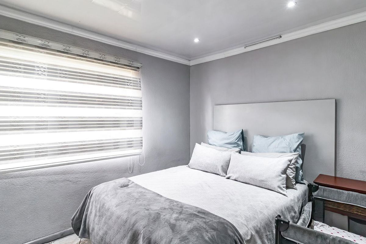 A well-maintained bedroom featuring a built-in headboard, recessed ceiling lighting, and modern zebra-style window blinds.