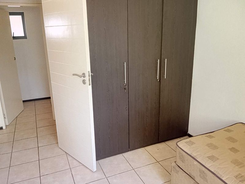 A bedroom featuring tiled flooring and a dark wood-finish built-in wardrobe with modern handles.