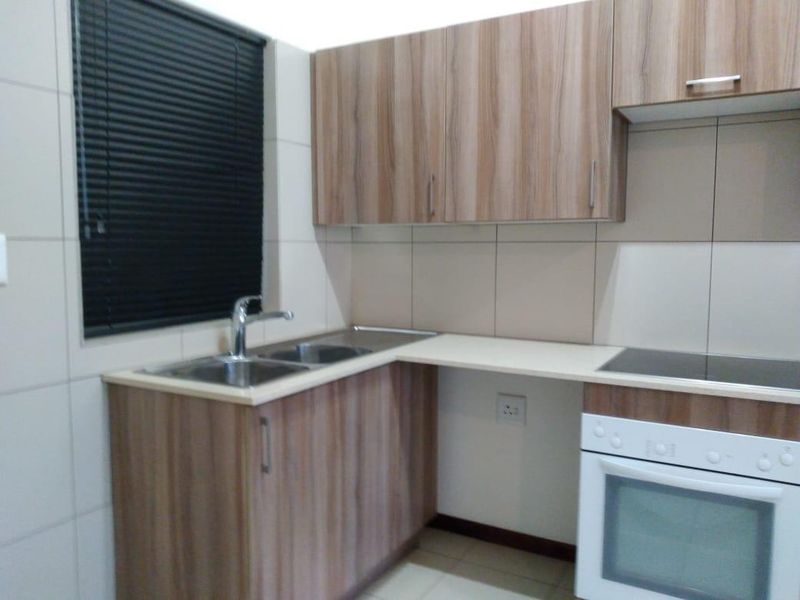A clean and functional kitchen featuring wood-look laminate cabinetry, a stainless steel double sink, built-in oven, and ceramic hob with tiled splashback.