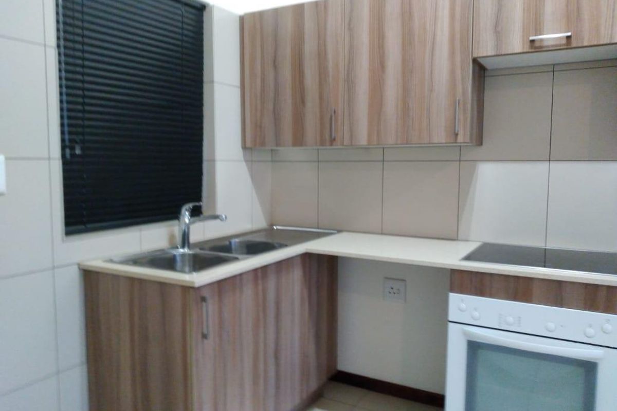 A clean and functional kitchen featuring wood-look laminate cabinetry, a stainless steel double sink, built-in oven, and ceramic hob with tiled splashback.