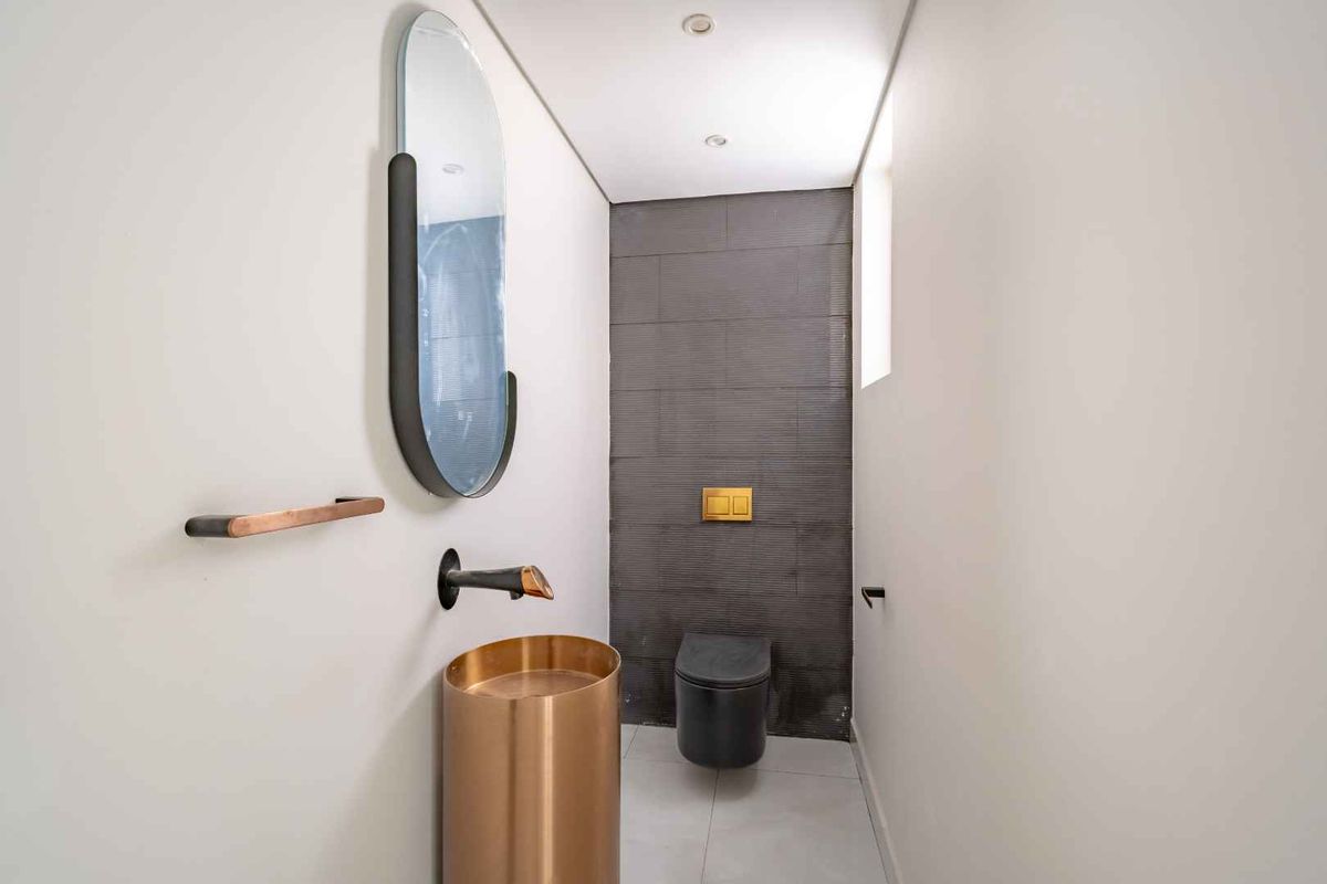 Modern powder room featuring a sleek pedestal basin, wall-mounted tapware, and a contemporary toilet with dark tiled feature wall.