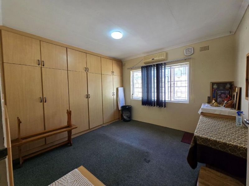 A bedroom featuring extensive built-in wooden cupboards, carpeted flooring, and an integrated air conditioning unit with security bars on the window.