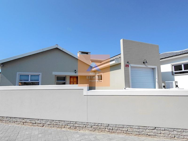 Front exterior view of a modern house featuring a paved driveway, secure boundary wall, and integrated garage.