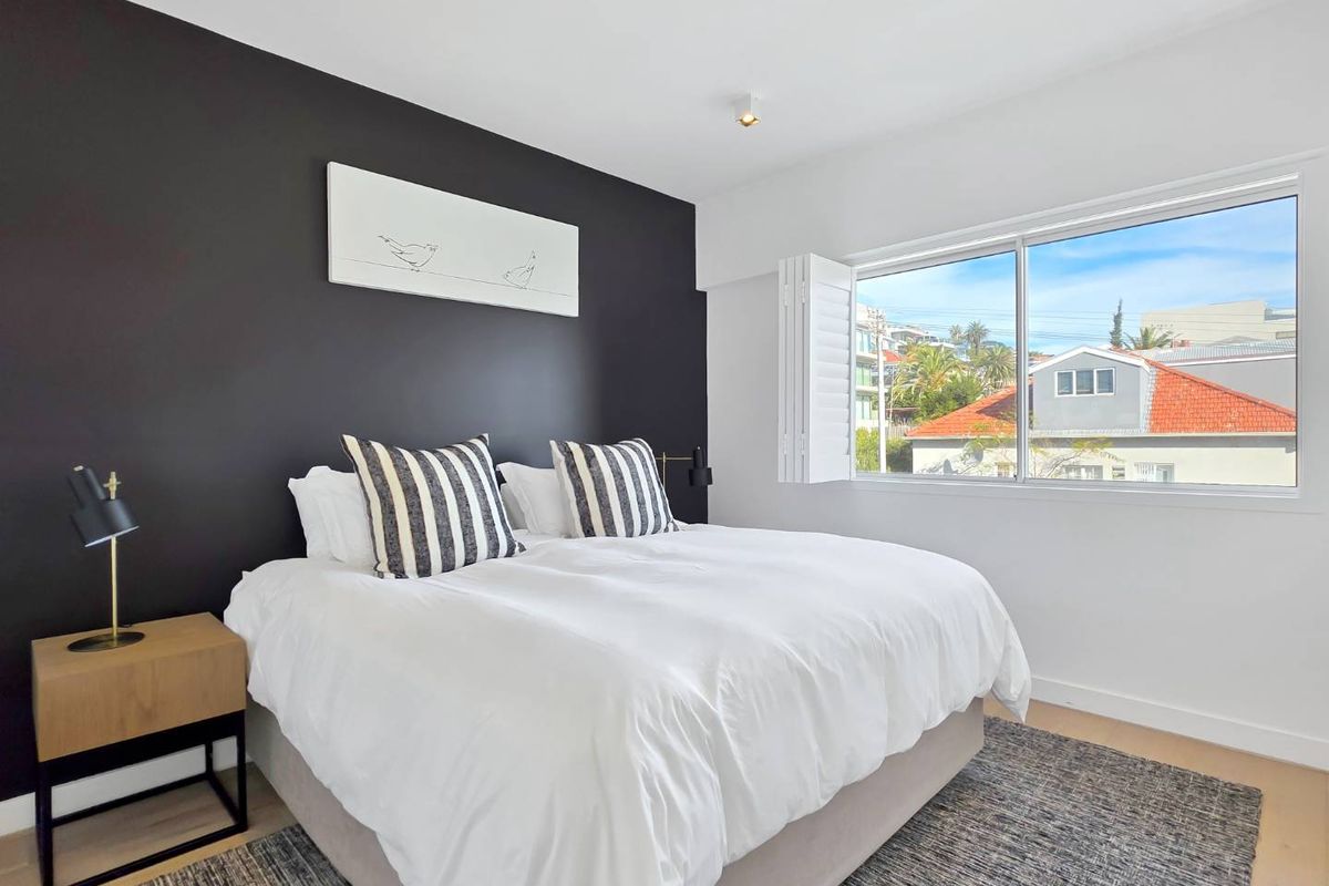 A well-maintained bedroom featuring a dark accent wall, timber flooring, and plantation shutters allowing natural light.