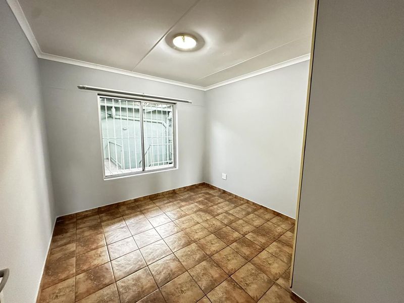 A clean, empty bedroom featuring neutral wall paint, ceramic tile flooring, and a window fitted with security bars.