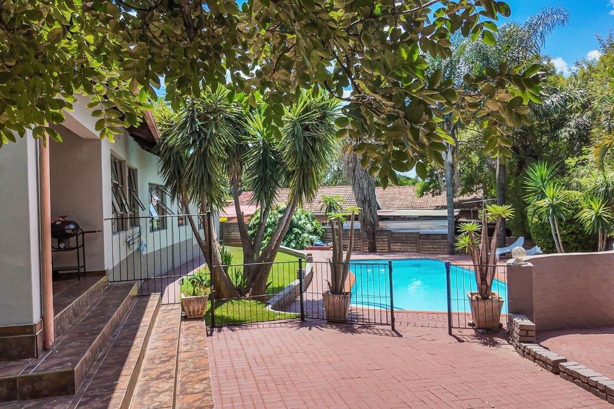 A spacious rear garden featuring a paved patio area, a swimming pool with safety fencing, and established trees.
