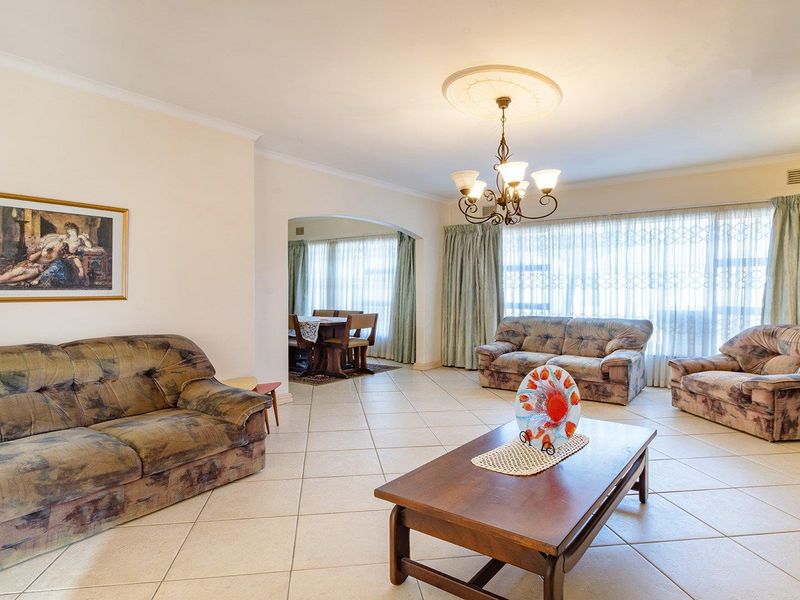 Spacious open-plan living and dining area featuring neutral tiled flooring, a decorative ceiling rose, and a classic archway connecting the two living spaces.
