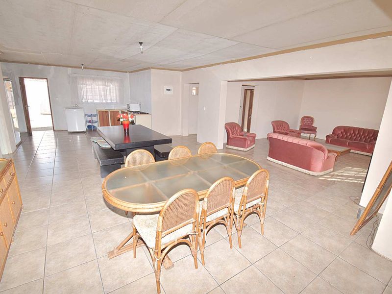 Spacious open-plan living and dining area featuring tiled flooring and a functional kitchen space, offering significant potential for modern renovation and layout optimization.