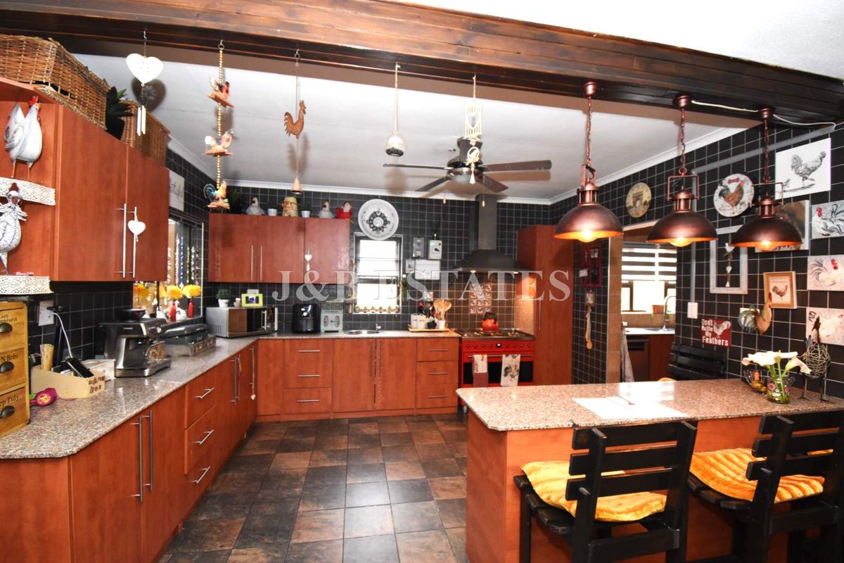 Spacious kitchen featuring wood-finish cabinetry, granite countertops, a central island, and a dedicated cooking area with a red stove and extractor fan.