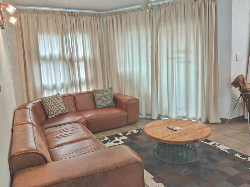 A living room area featuring tiled flooring and a ceiling fan, with large windows covered by floor-to-ceiling curtains.