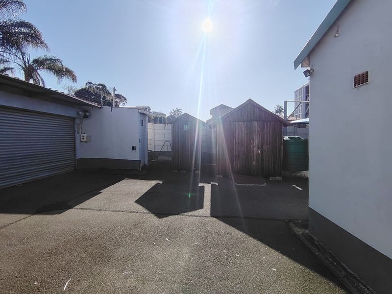 Rear exterior area featuring an asphalt driveway, roller shutter door access, and two wooden storage sheds with a water tank.