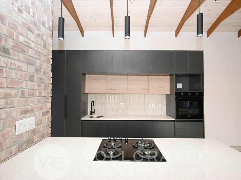 Modern kitchen featuring dark cabinetry, stone countertops, integrated gas hob, built-in oven, and striking exposed brick and timber beam ceiling details.