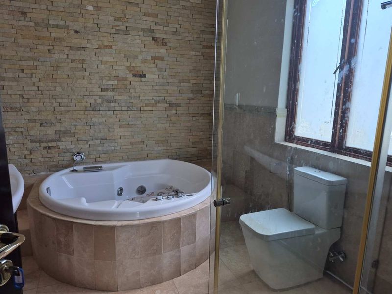 A bathroom featuring a built-in jetted bathtub with stone tile surround, a glass-enclosed shower area, and a toilet.