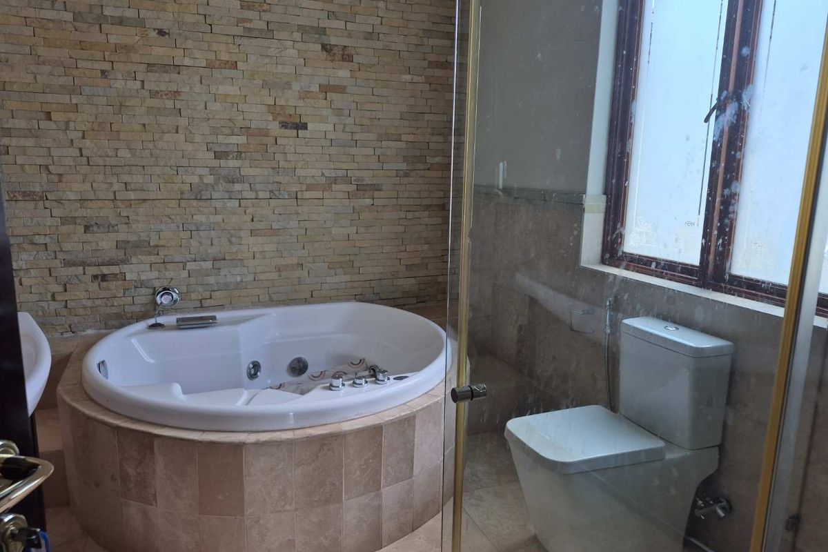 A bathroom featuring a built-in jetted bathtub with stone tile surround, a glass-enclosed shower area, and a toilet.