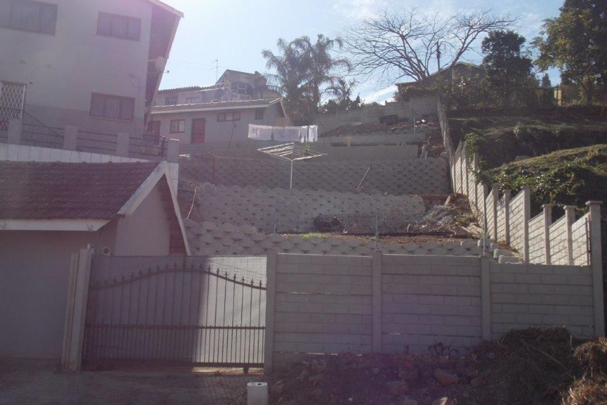 Rear exterior view of the property featuring a multi-level terraced garden with concrete retaining walls and perimeter fencing.