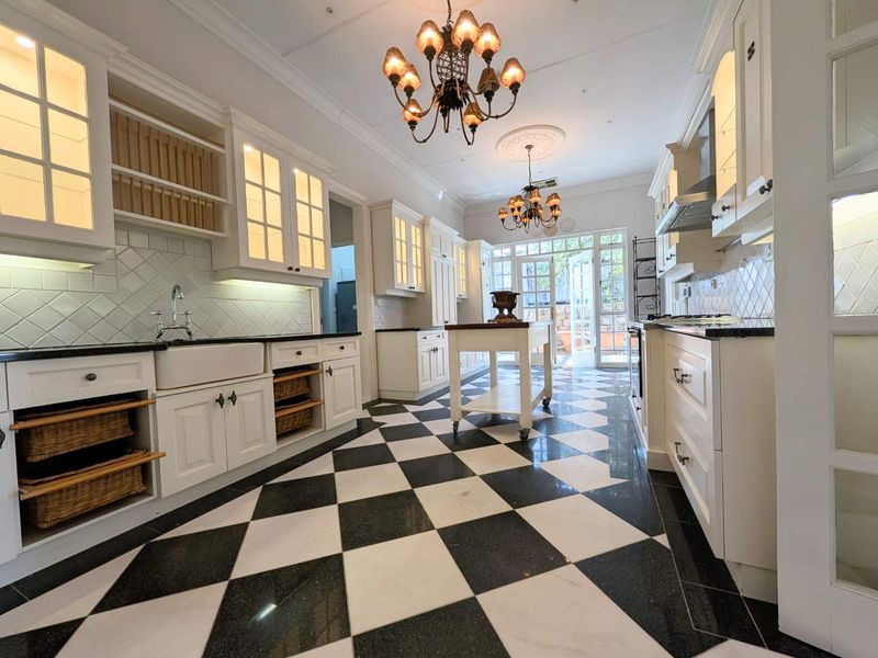 Elegant kitchen featuring classic checkerboard marble flooring, custom white cabinetry, farmhouse sink, and high-end finishes with direct access to the outdoor area.