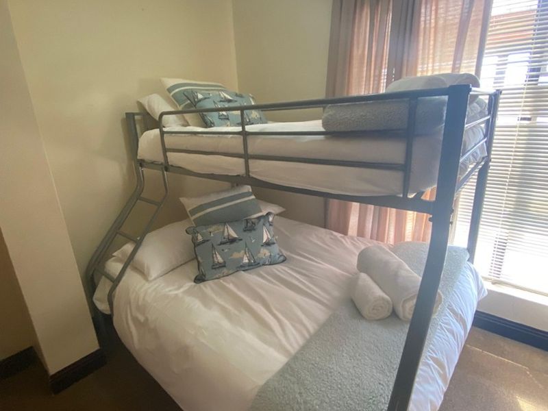 A compact bedroom featuring neutral walls, carpeted flooring, and a window with fitted blinds and curtains.