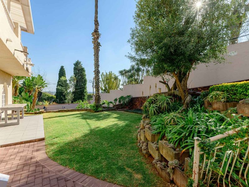 A rear garden area featuring a paved patio, tiered landscaping with retaining walls, and a well-maintained lawn.